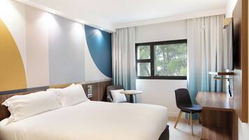 A hotel room with a large bed, a desk, a chair, and a window with a view of trees.
