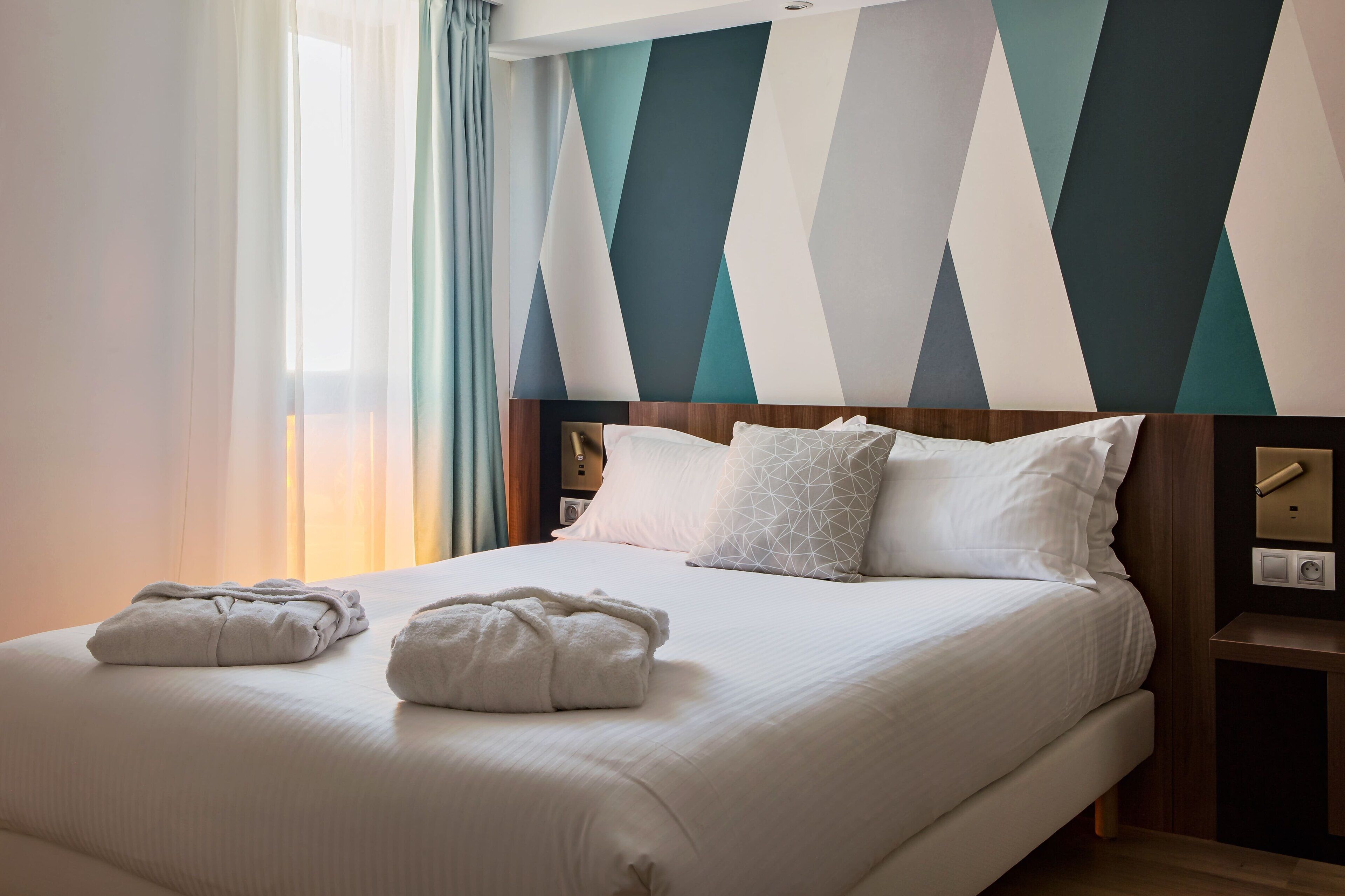 Habitación de hotel con una cama, almohadas, una mesita de noche y una pared con diseños geométricos.