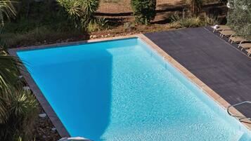 A rectangular swimming pool with clear blue water, surrounded by a deck area with lounge chairs and umbrellas.