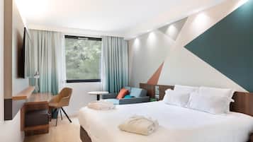 A modern hotel room with a large bed, a desk with a chair, a small table, and a TV mounted on the wall.