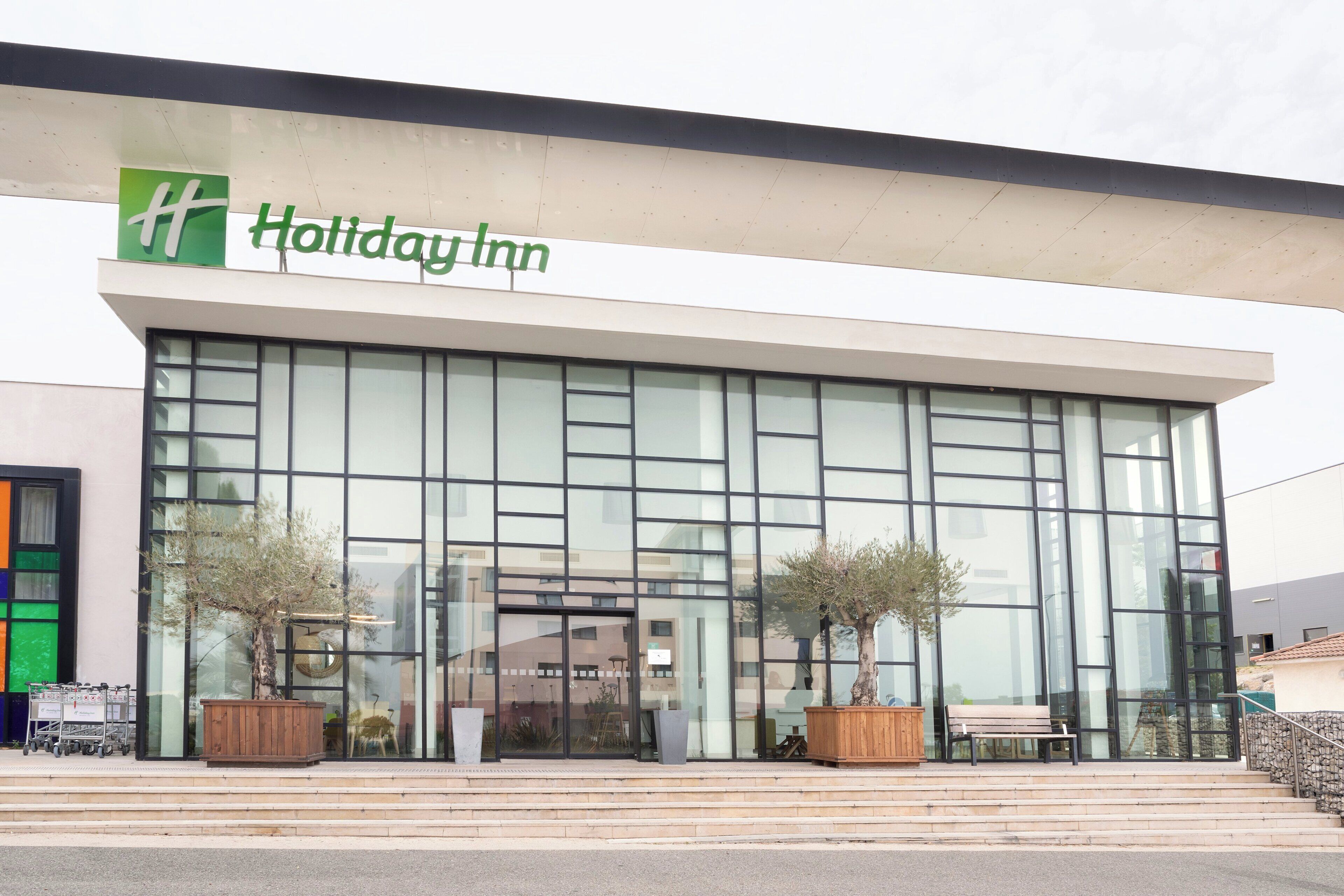 A Holiday Inn hotel with a modern facade, large windows, and outdoor seating.