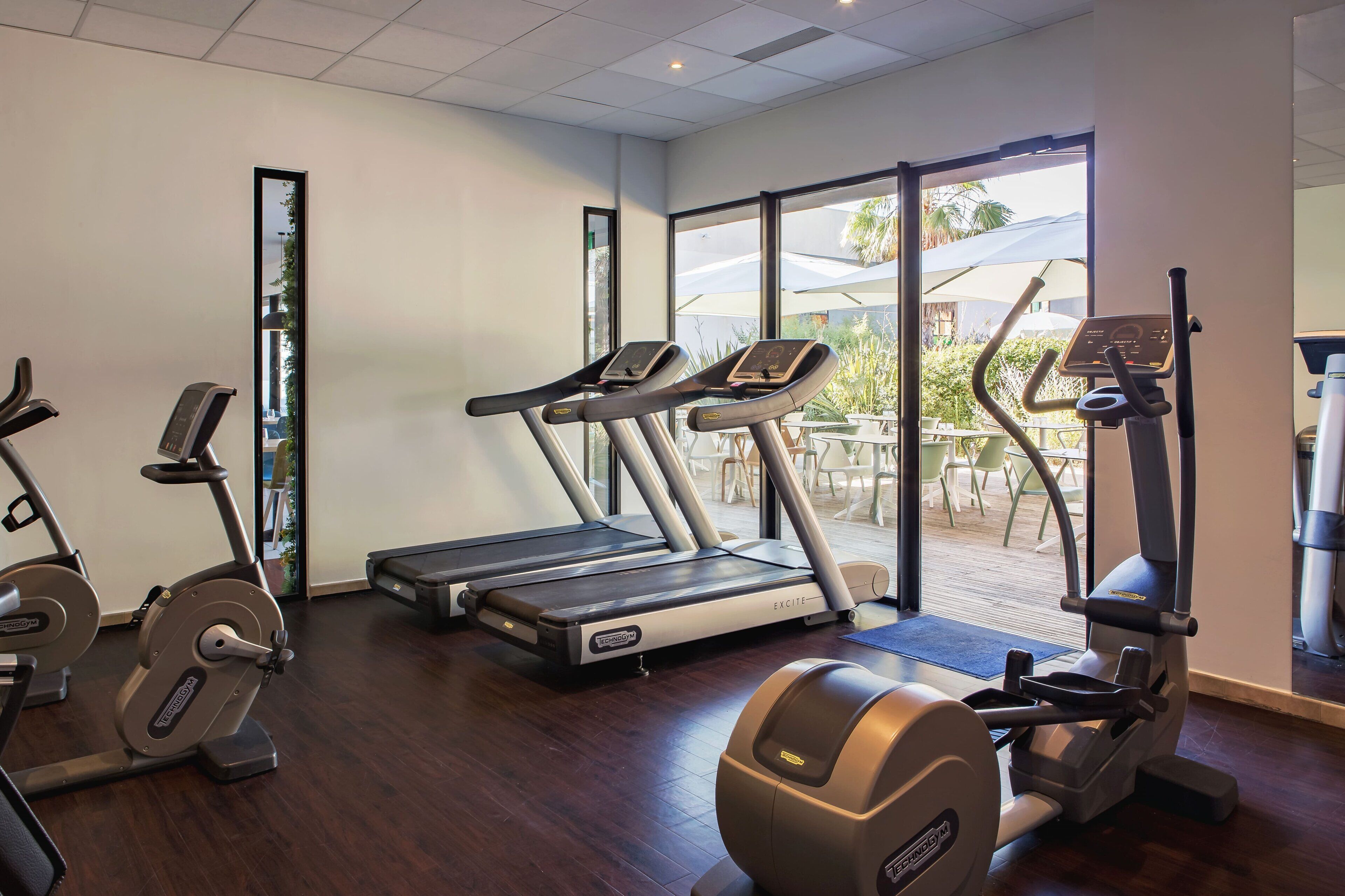 A gym with various exercise machines, a large window, and a view of the outdoors.