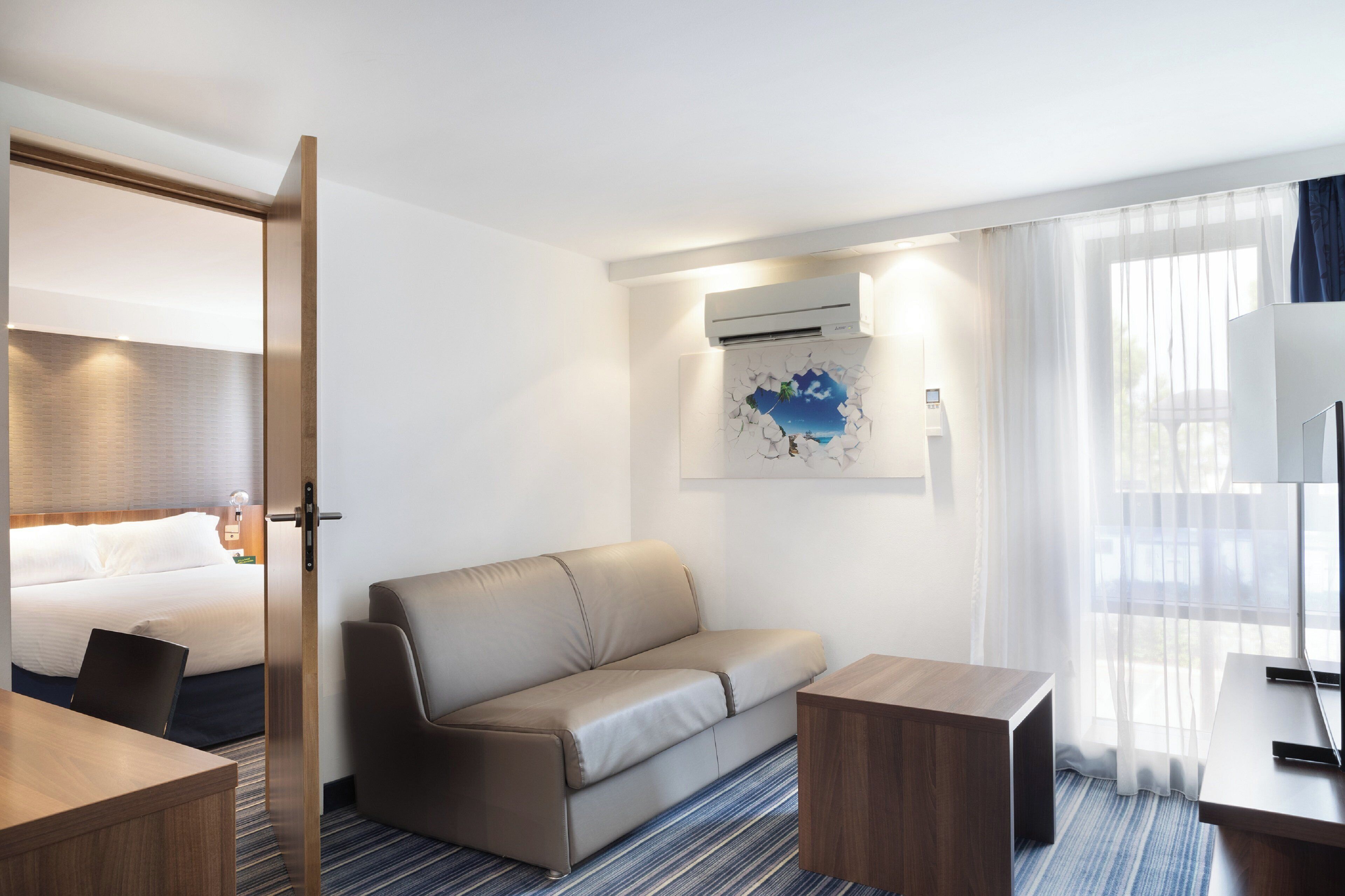 A hotel room with a bed, a sofa, a small table, and a desk.