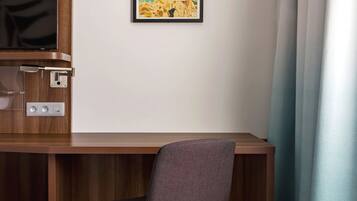 A wooden desk with a chair, a framed picture on the wall, and a power outlet with switches.