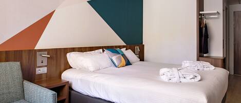 A modern hotel room with a large bed, a wooden headboard, a grey sofa, and a wooden nightstand.