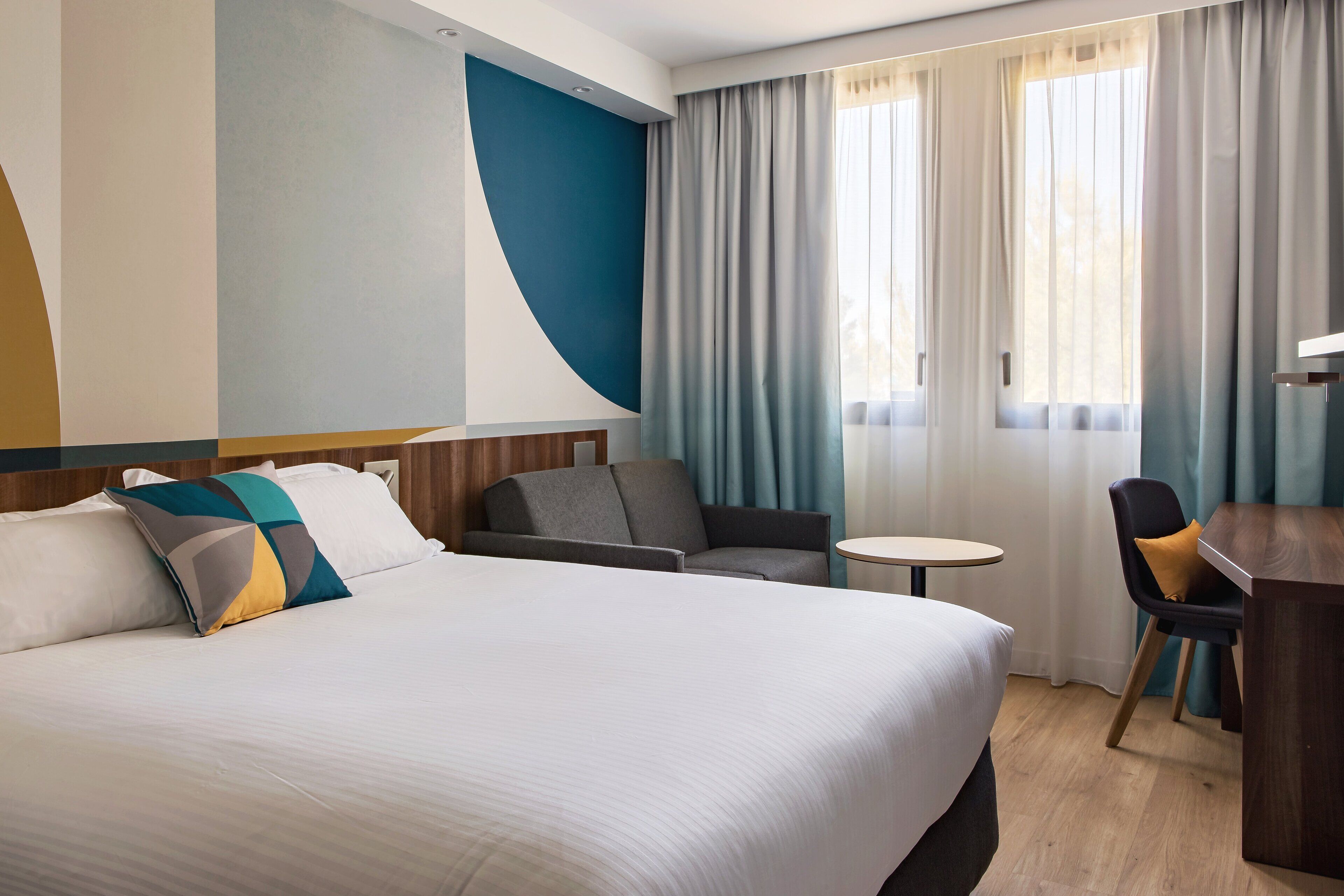 A hotel room with a large bed, a small round table, a sofa, and a desk.