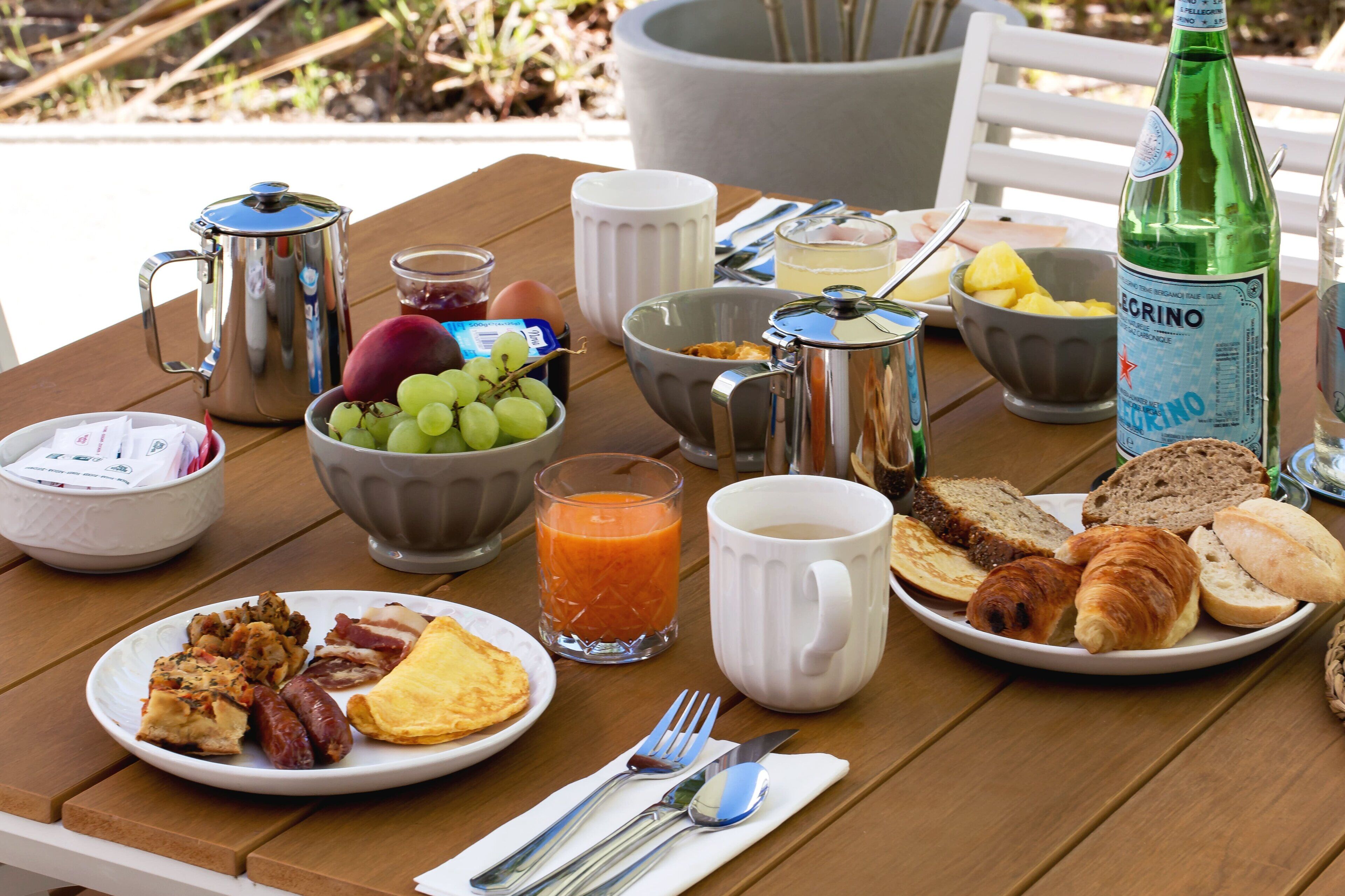 Une table de petit-déjeuner avec une variété d’aliments, notamment des œufs, des toasts et des viennoiseries, ainsi qu’une bouteille d’eau et une cafetière.
