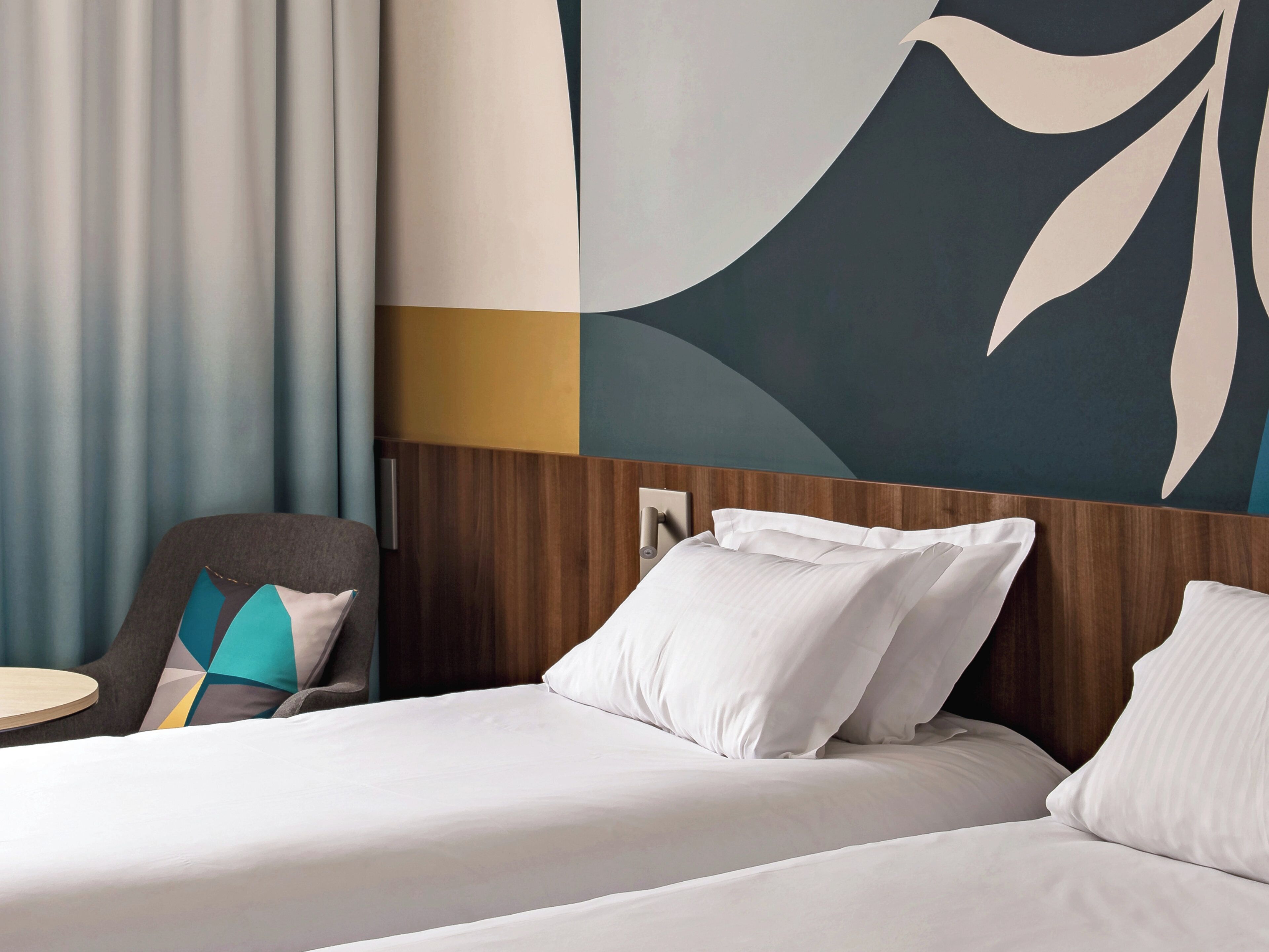 A hotel room with a bed, a chair, and a wall with abstract art.