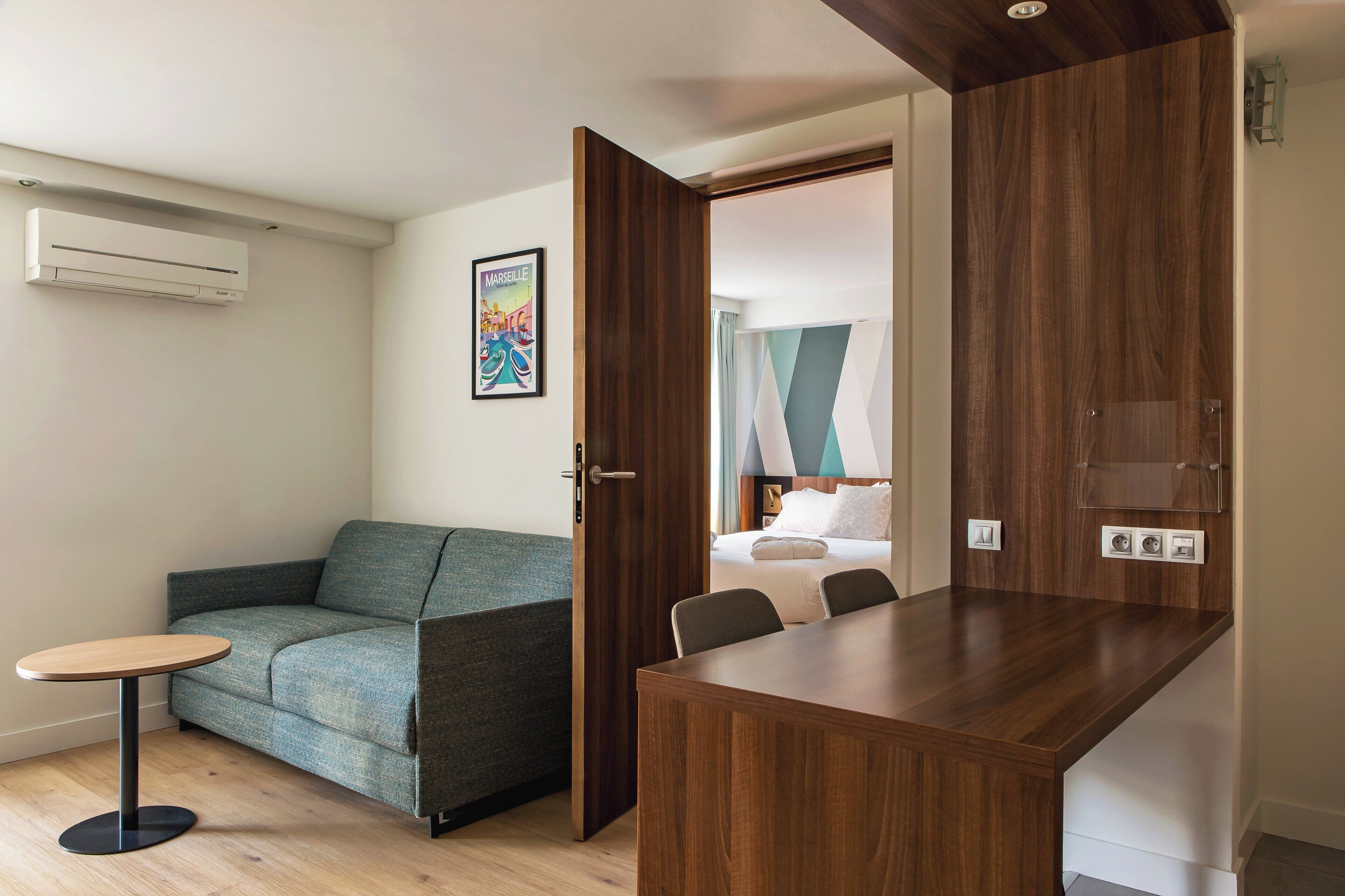 A hotel room with a sofa, a small round table, a wooden desk, and a bed with a view.