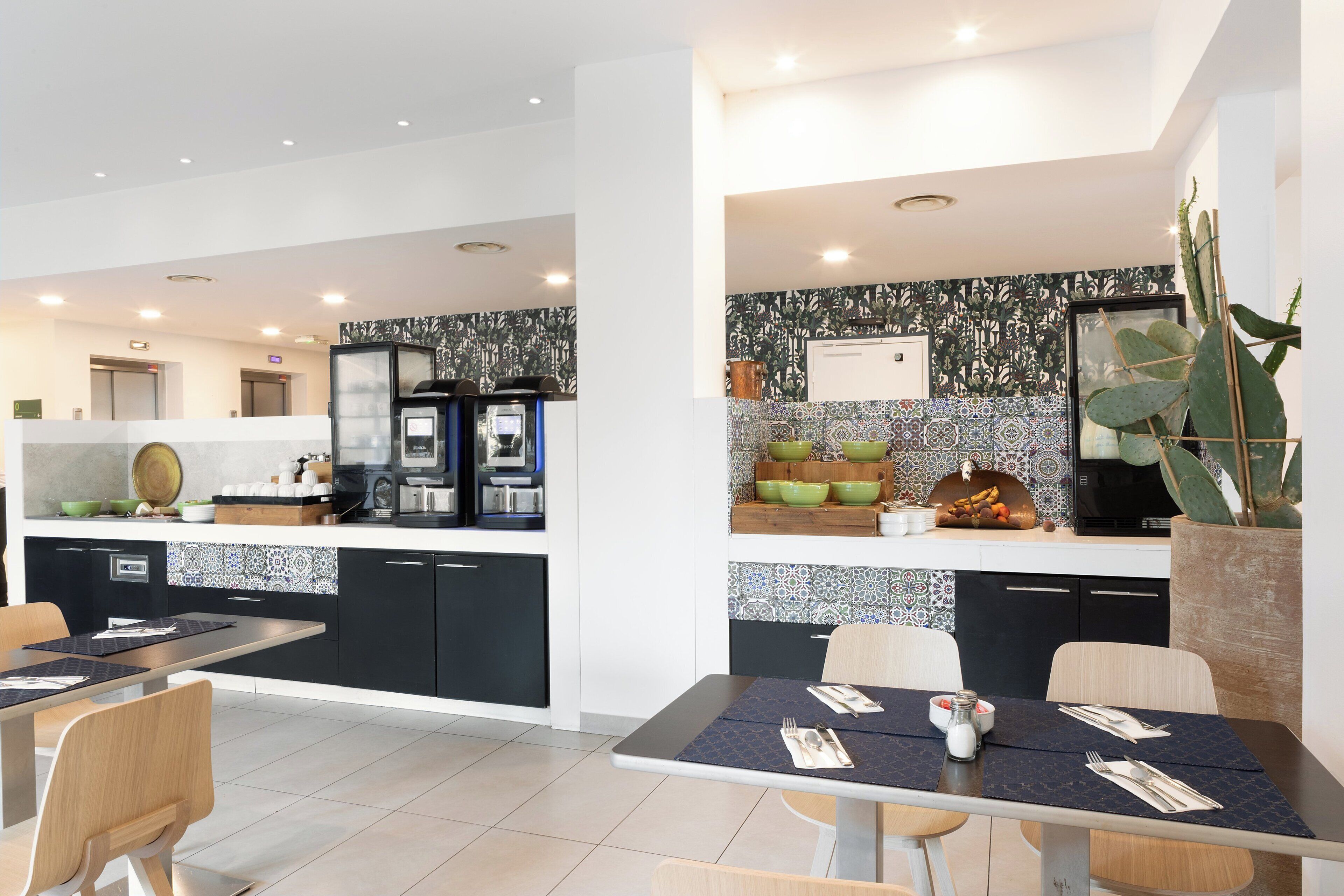 A modern kitchen with a central island, a dining area with a table set for two, and a large cactus plant.