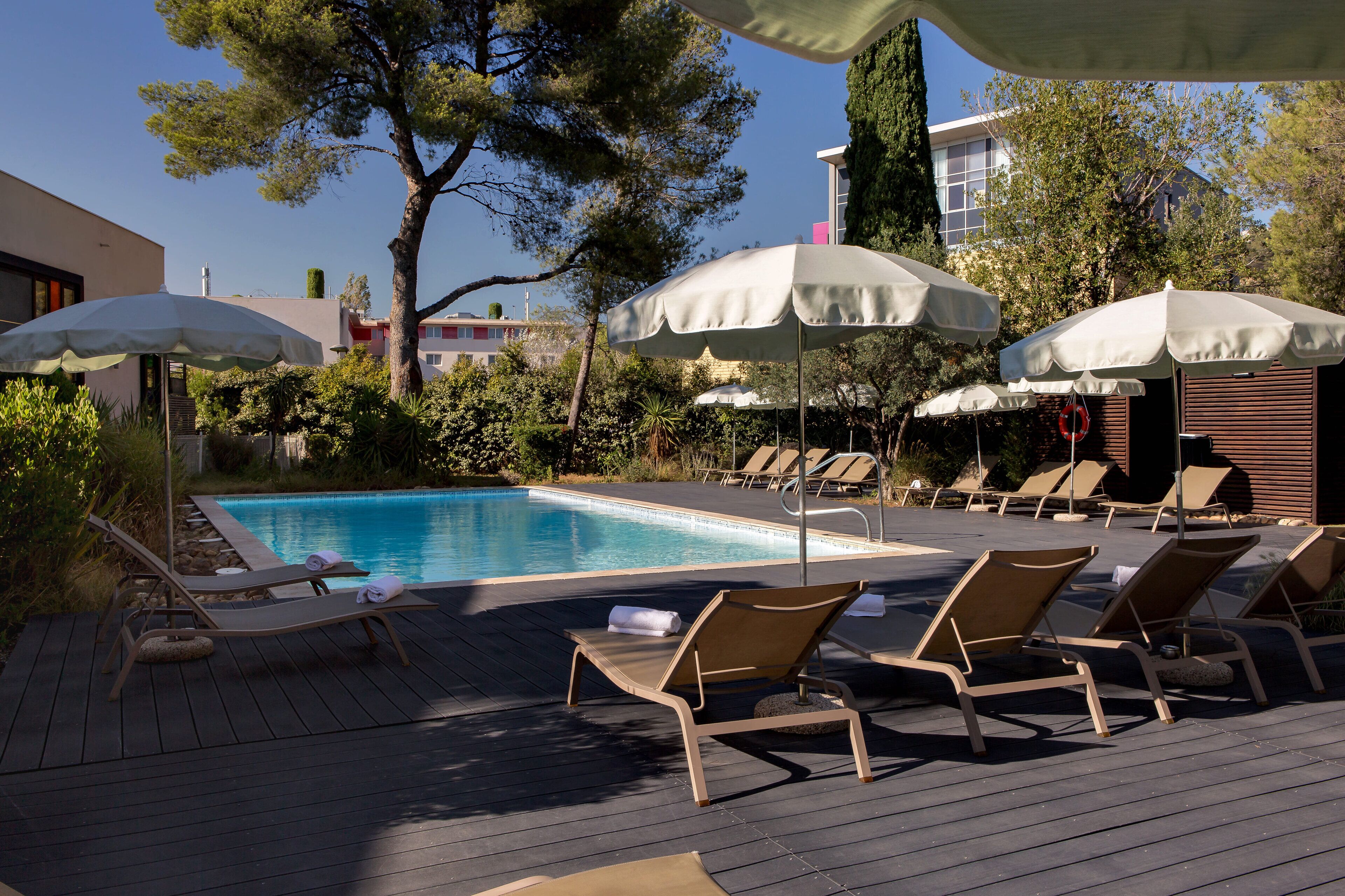 Una piscina al aire libre, sombrillas, sillones reclinables de piscina