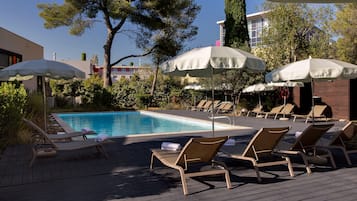 Una piscina al aire libre, sombrillas, sillones reclinables de piscina
