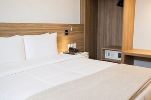 A hotel room with a wooden headboard, a white bedspread, a bedside table with a phone and books, and a control panel. - Intercity Gravataí (Gravatai)