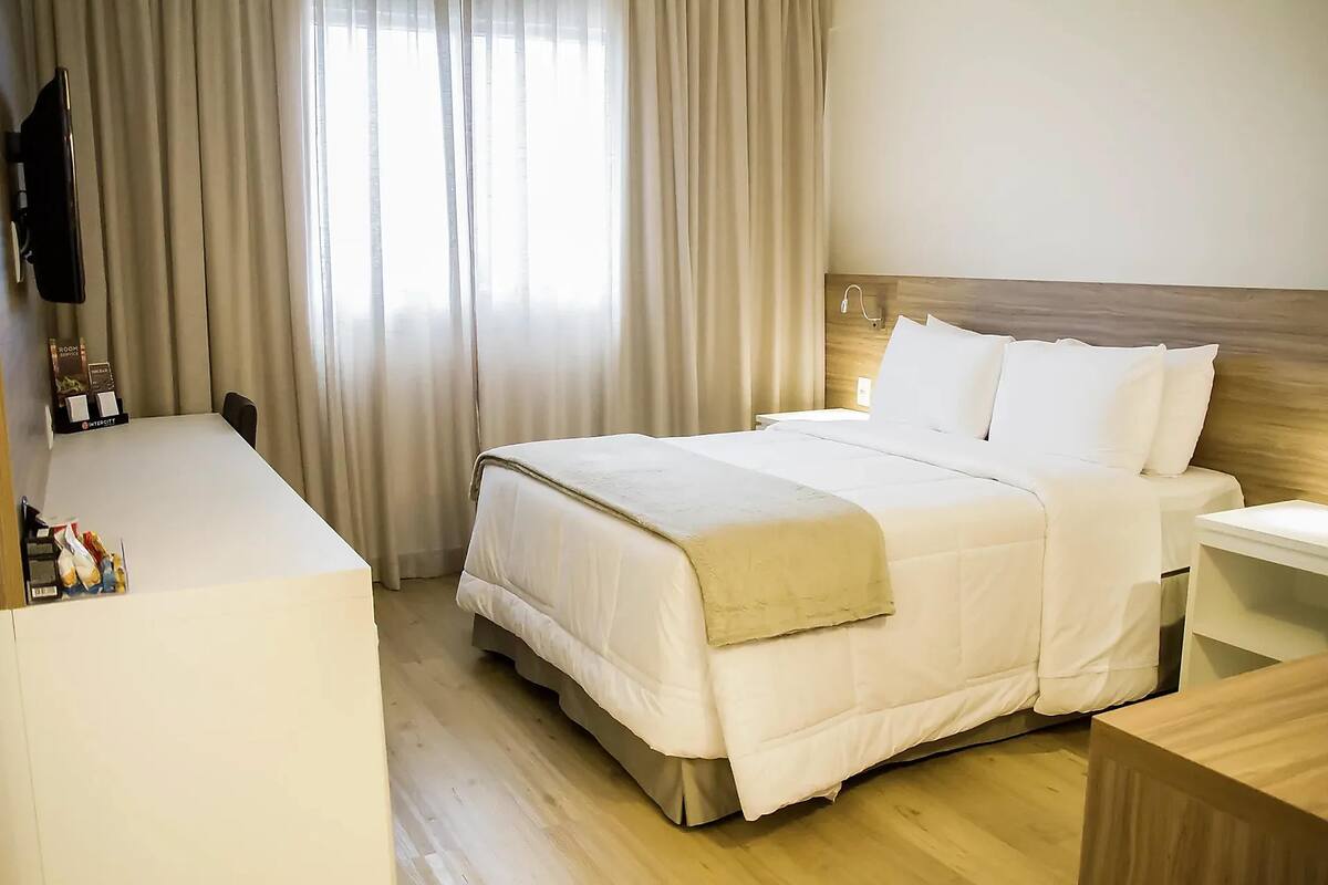 Una habitación de hotel con cama, mesita de noche y escritorio con televisor de pantalla plana.