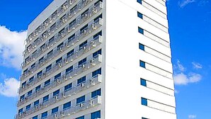 Ein mehrstöckiges Hotel mit weißer Fassade, zahlreichen Fenstern und einem auffälligen, orangefarbenen Schild, das den Namen des Hotels angibt.