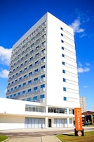 Hotel de vários andares com fachada branca, inúmeras janelas e um letreiro laranja bem visível com o nome do hotel.