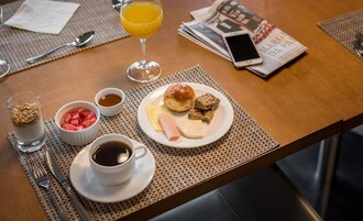 Uma mesa de café da manhã com um prato de comida, um copo de suco de laranja, uma xícara de café e um jornal.