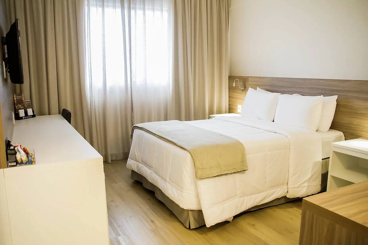 Habitación de hotel con cama, mesita de noche y escritorio con televisor de pantalla plana.