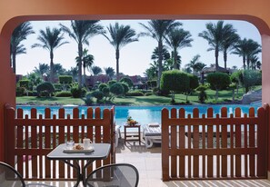 Un espace aménagé au bord de la piscine, offrant une vue sur la piscine, les palmiers et un terrain de golf.