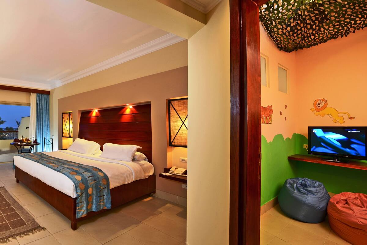 A hotel room with a bed, a desk with a computer, a television, and a balcony with a view of the city.