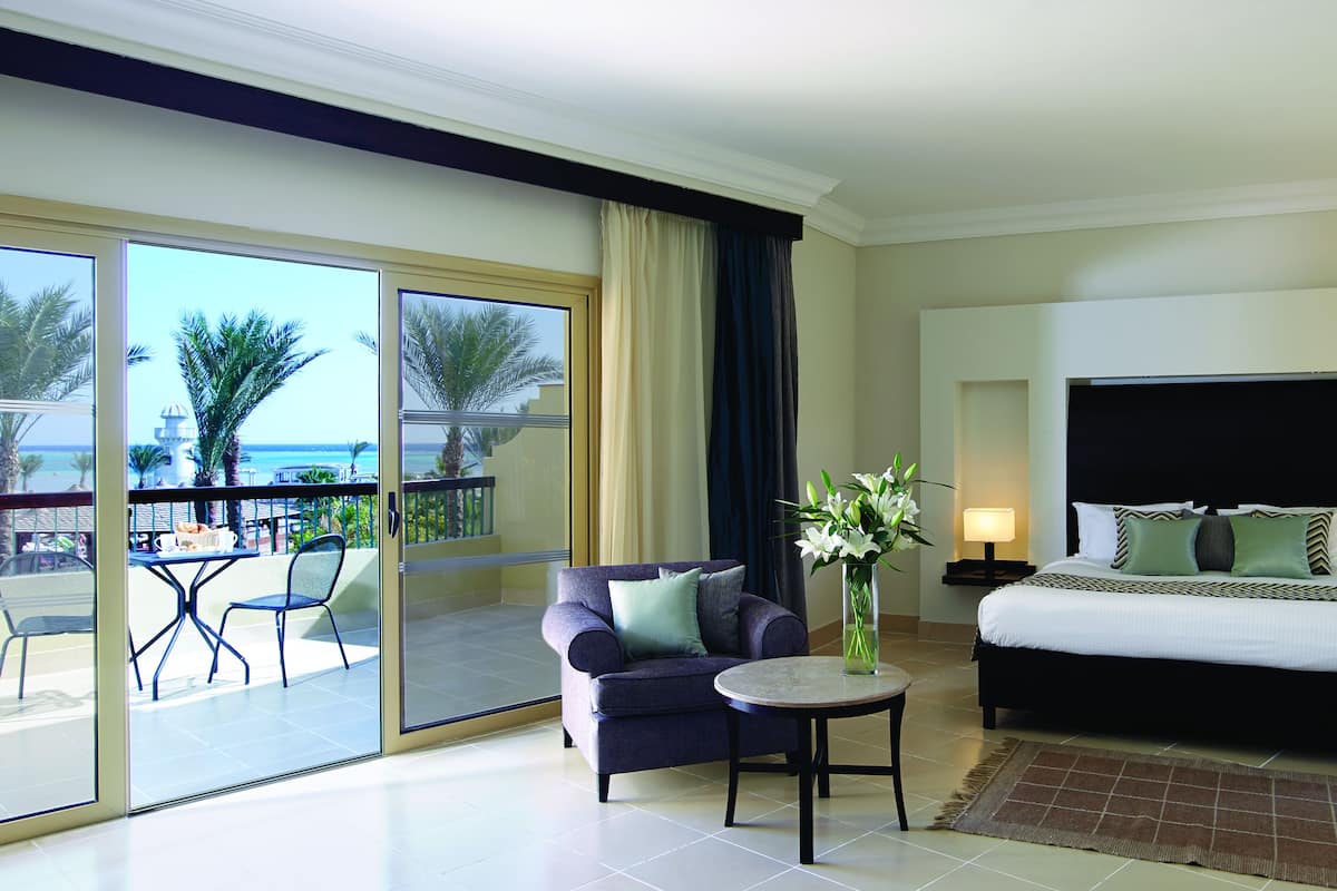 A hotel room with a balcony, a bed, a sofa, and a small table.