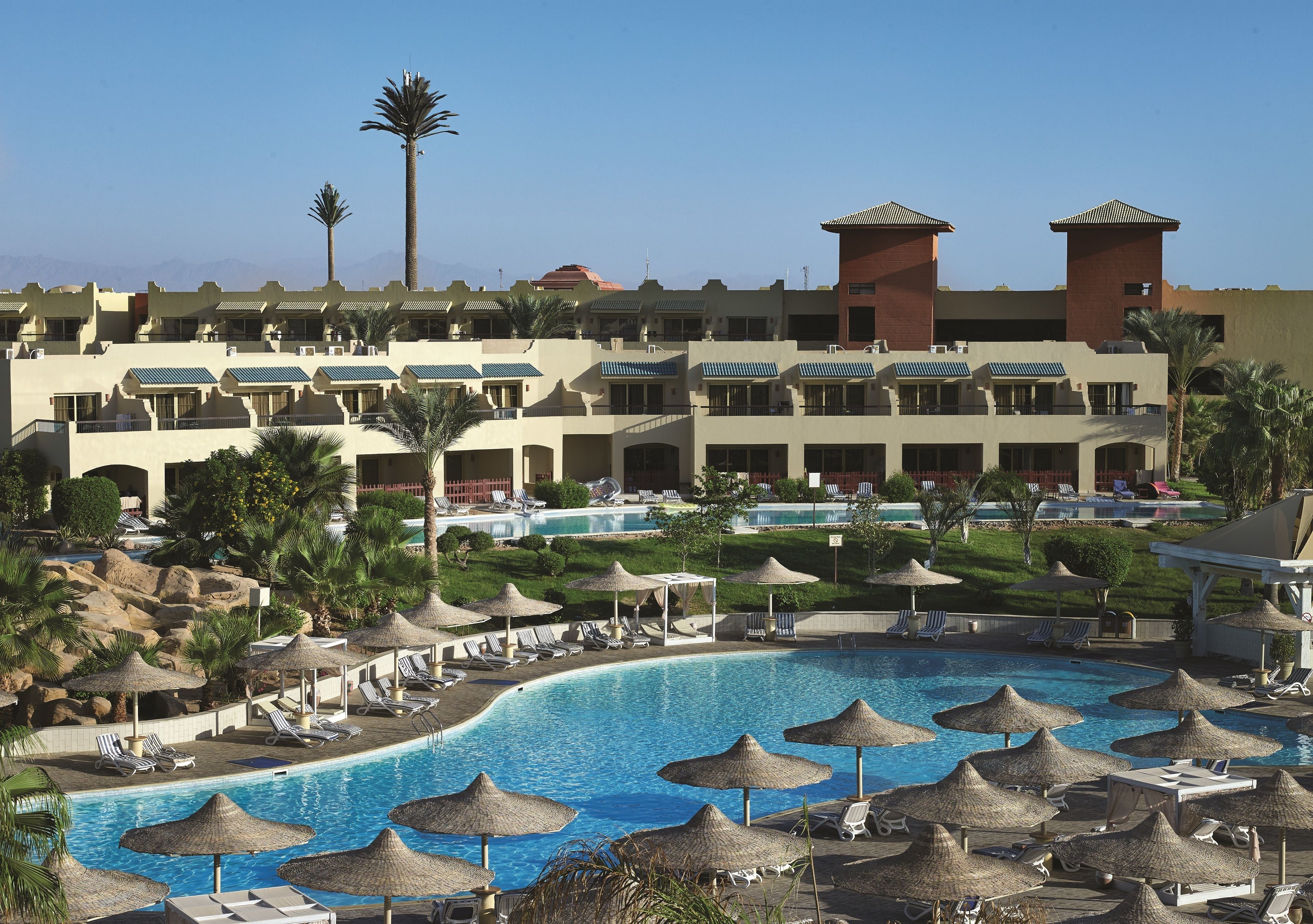 Ein Resort mit großem Pool, Liegestühlen, Sonnenschirmen und einem Gebäude mit mehreren Balkonen.