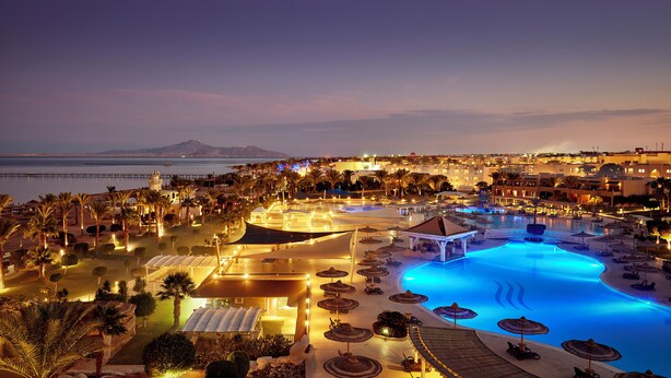 Un resort con una amplia piscina, palmeras y vista al mar.