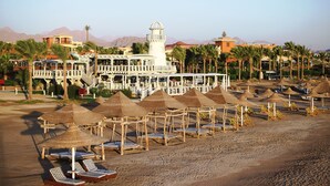Un resort con varias edificaciones, palmeras y una playa con tumbonas y sombrillas.