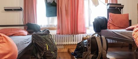 Une chambre avec deux lits, un radiateur, une fenêtre avec des rideaux et un bureau avec une lampe.