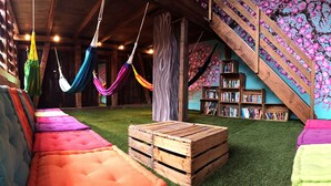 A cozy room with a wooden staircase, colorful cushions, a hammock, and a bookshelf. - Balmers Hostel (Matten bei Interlaken)