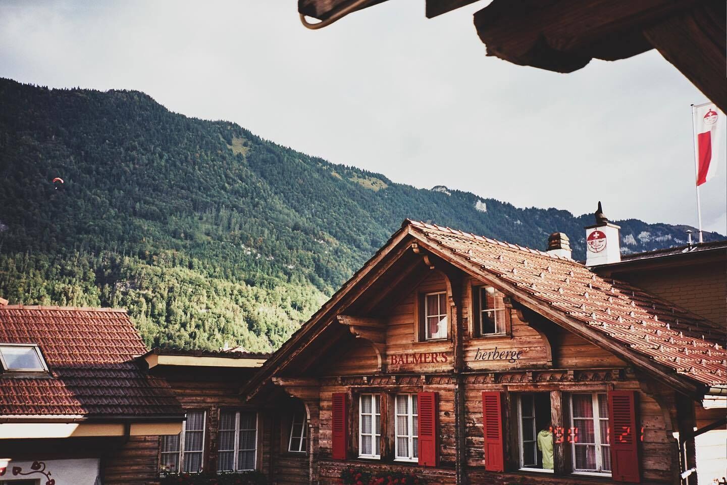 A wooden building with a sloped roof, labeled "BALMER'S," set against a mountainous backdrop. - Balmers Hostel (Matten bei Interlaken)