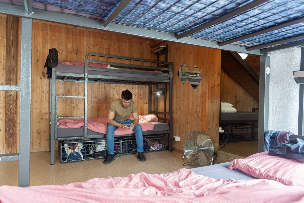 Habitación con literas, ventilador, paredes de madera y tragaluz.