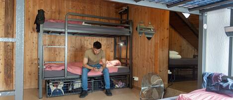 Habitación con literas, ventilador, paredes de madera y tragaluz.
