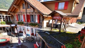 A wooden building with a sign that reads "BALMER'S Barbeque" and outdoor seating with umbrellas. - Balmers Hostel (Matten bei Interlaken)