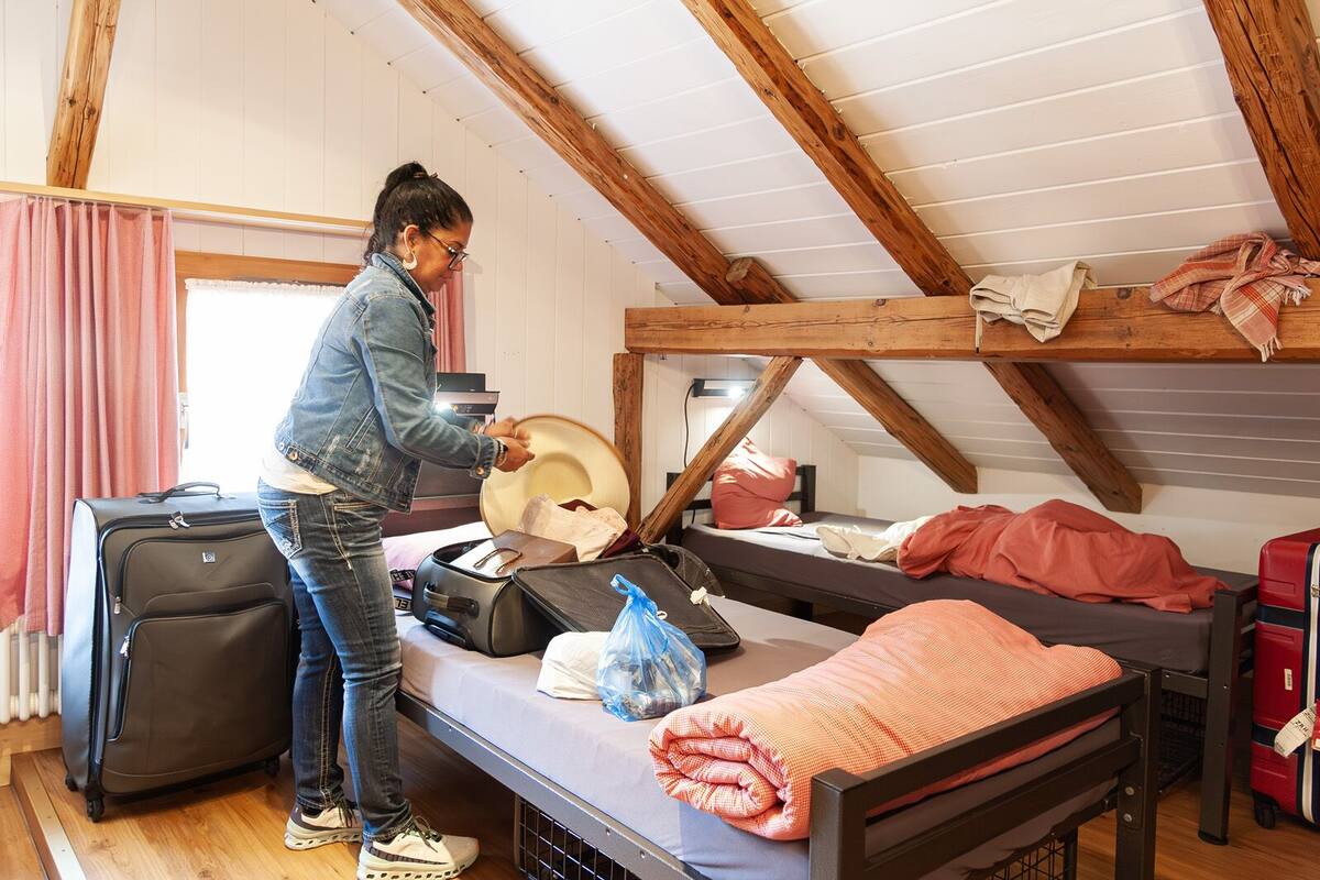 Una habitación con una litera, una maleta y una maleta con ruedas, además de una cama con una colcha.