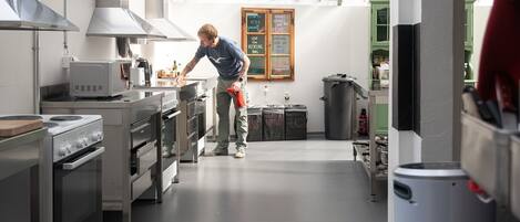 A modern kitchen with stainless steel appliances, a chalkboard with recycling instructions, and a person cleaning.