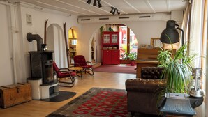 A cozy living room with a fireplace, red armchair, and a large potted plant. - Balmers Hostel (Matten bei Interlaken)