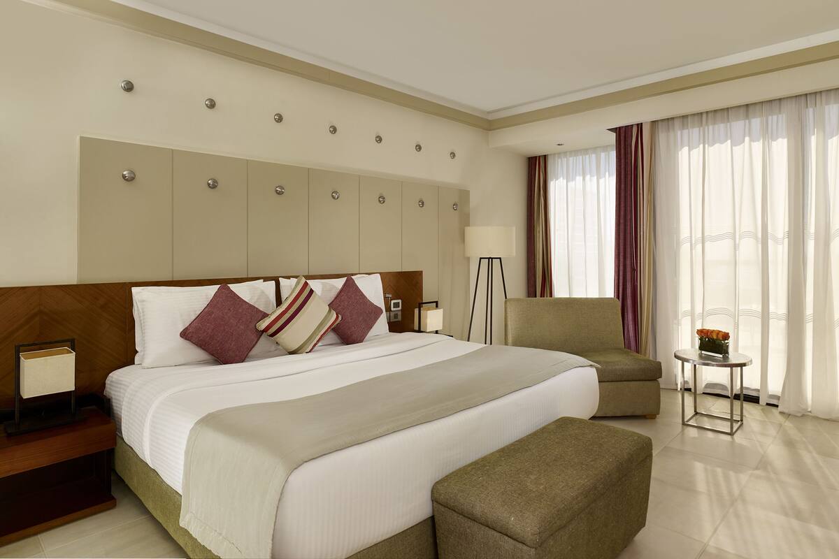 A hotel room with a large bed, a sofa, a small table, and a desk.