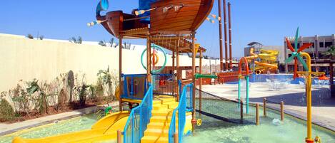 Parque acuático con una estructura de barco de madera, un tobogán amarillo y una zona de piscina.