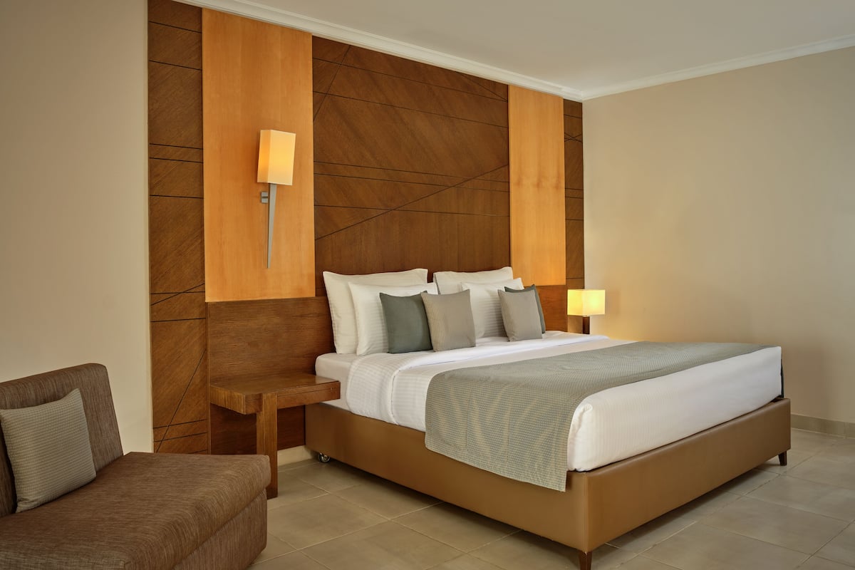 A modern hotel room with a large bed, a bedside table, a chair, and a wall-mounted lamp.