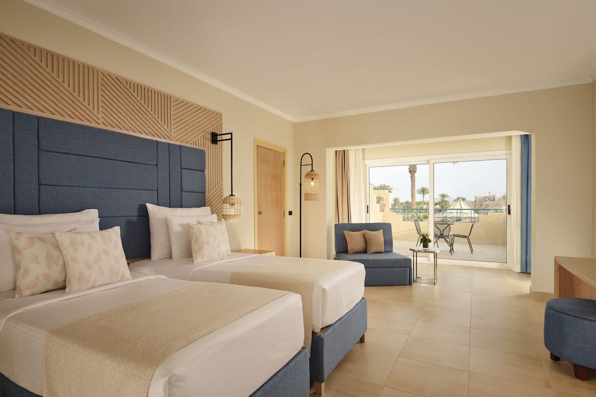 A hotel room with two beds, a sofa, a small table, and a balcony with a view.