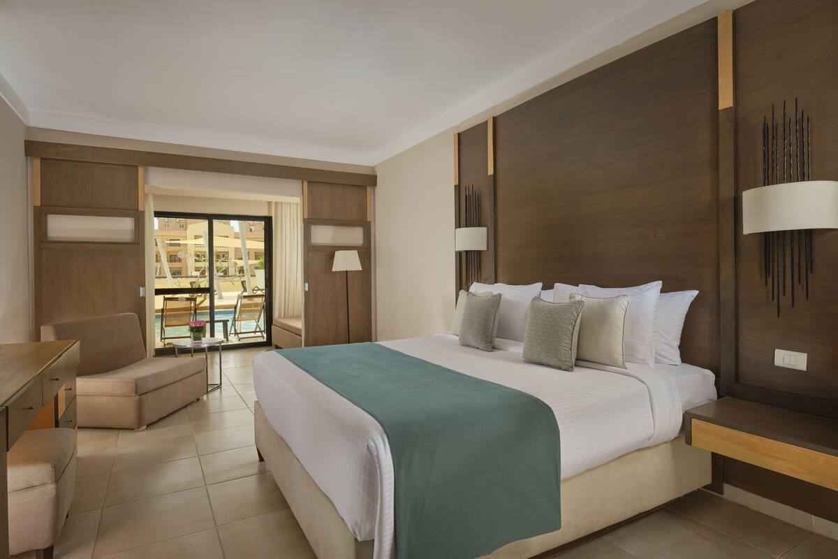 Hotelkamer met een groot bed, een bureau, een stoel en uitzicht op het zwembad.