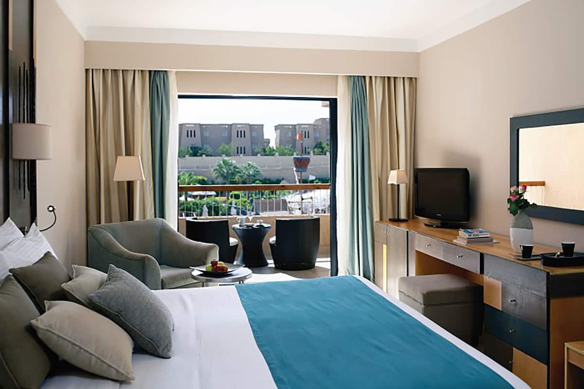 Een hotelkamer met een groot bed, een bureau met een televisie, een stoel en uitzicht op gebouwen.