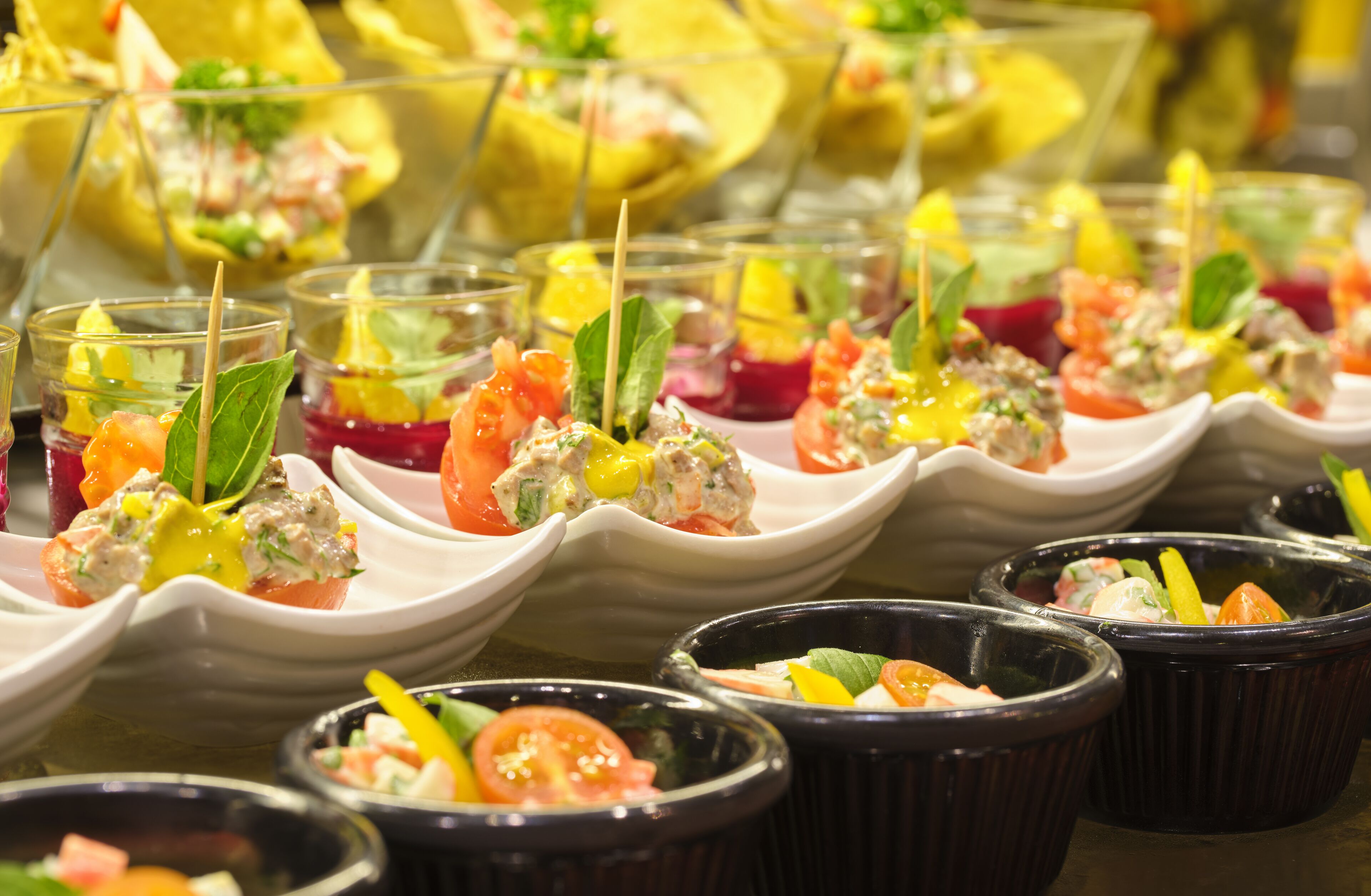 Una variedad de aperitivos dispuestos en una mesa, incluyendo brochetas y recipientes pequeños con ensaladas y salsas coloridas.