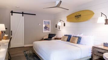 A hotel room with a bed, a desk, a chair, a ceiling fan, and a surfboard decoration.