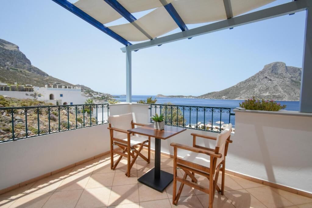 Un balcón con mesa y sillas, vista al mar y paisaje montañoso.