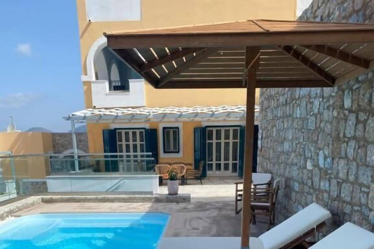 A rooftop pool area with lounge chairs, a pergola, and a stone wall.