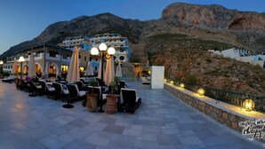 A seaside terrace with outdoor seating, a mountain backdrop, and a view of the sea. - Elena Village (Kalymnos)