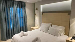 A hotel room with a large bed, a nightstand, a lamp, and a window with curtains. - Elena Village (Kalymnos)