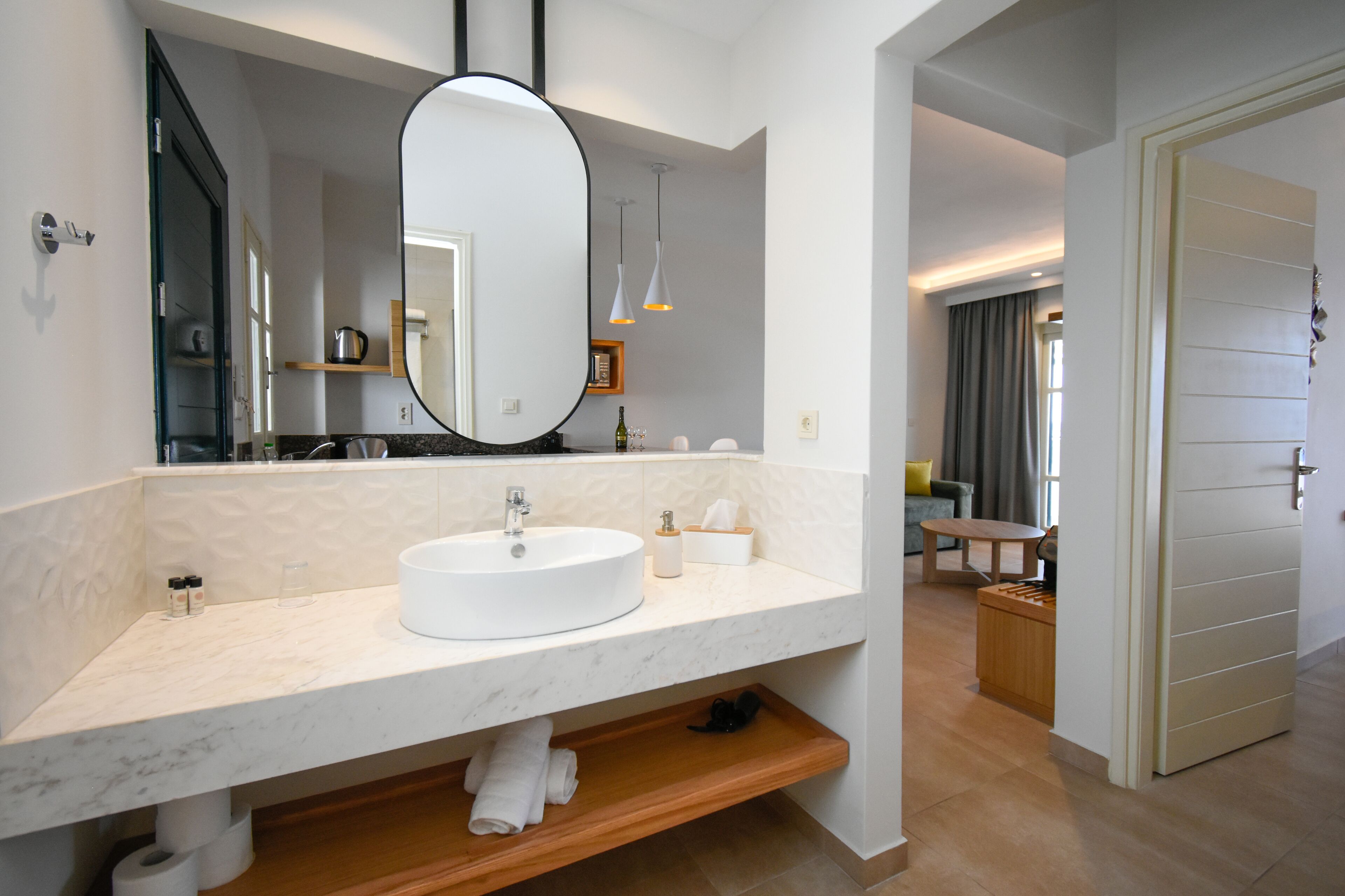 A modern bathroom with a large oval mirror, a white sink, and a wooden shelf.